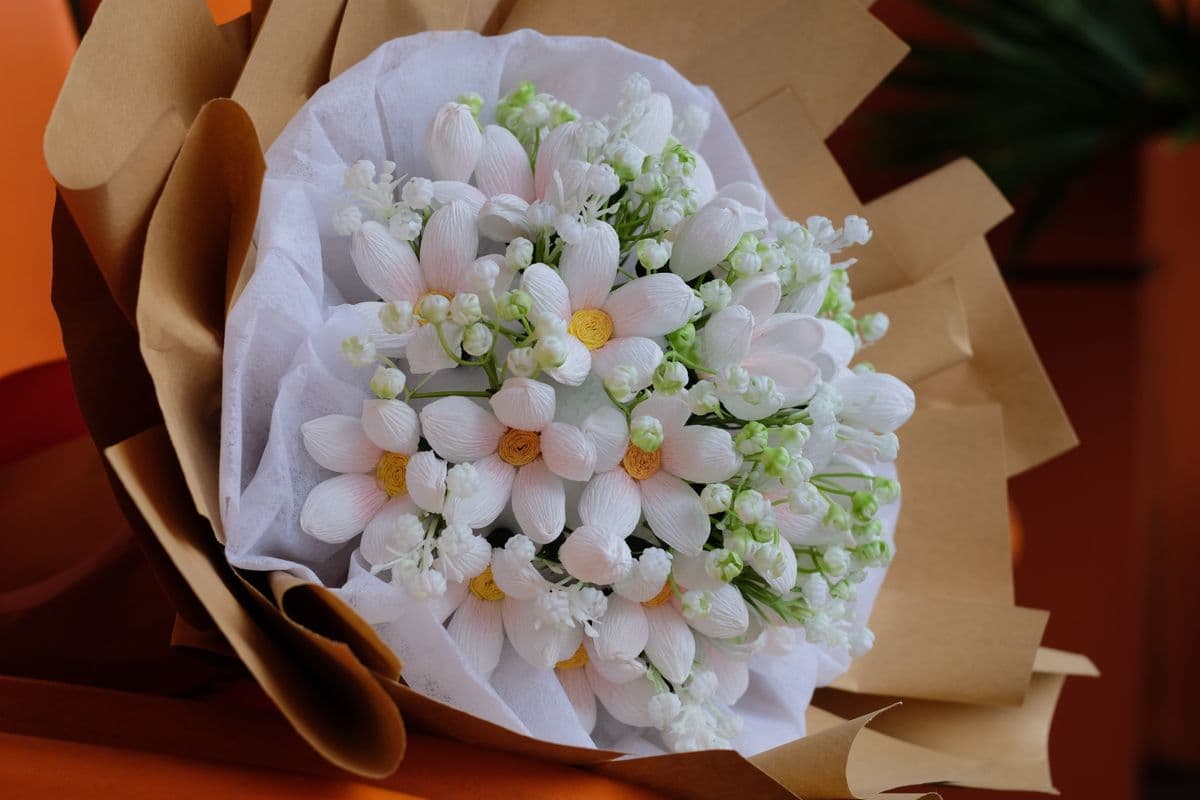 A round bouquet of small white flowers wrapped in white tissue and kraft paper