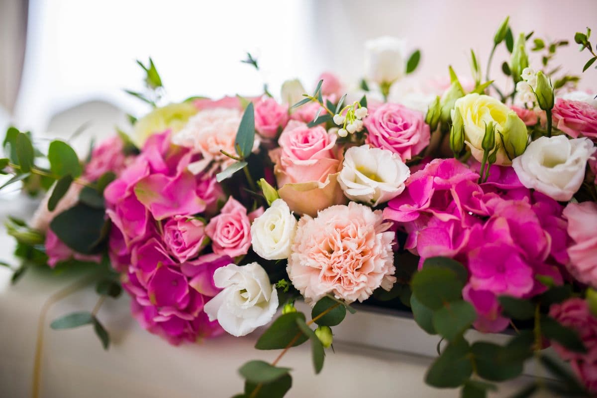 Pink hydrangeas, roses and carnations arranged low in a white vessel