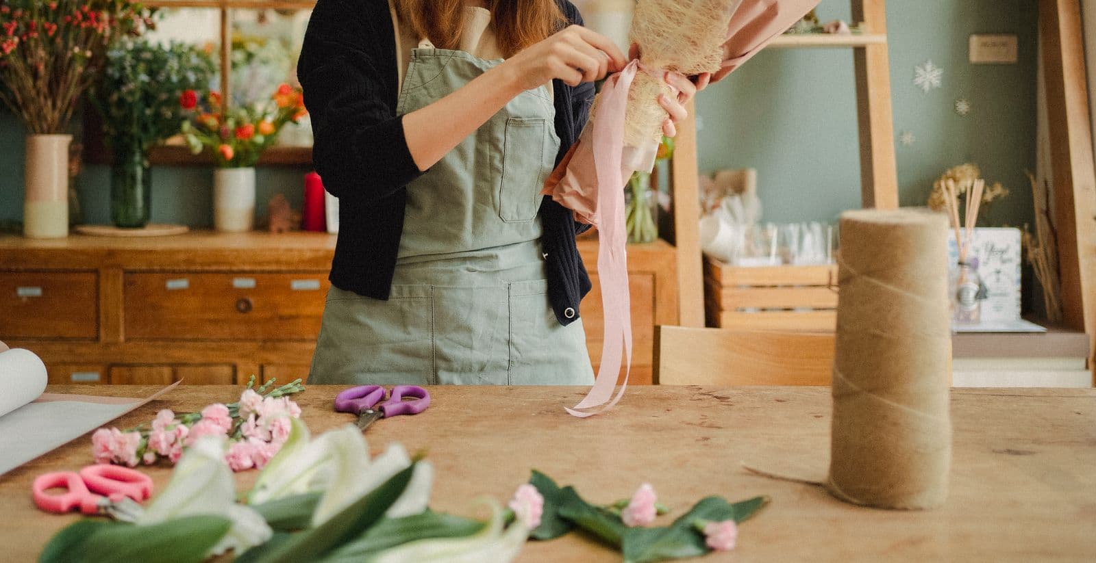 A florist tying a ribbon around a bouquet at a wooden work table